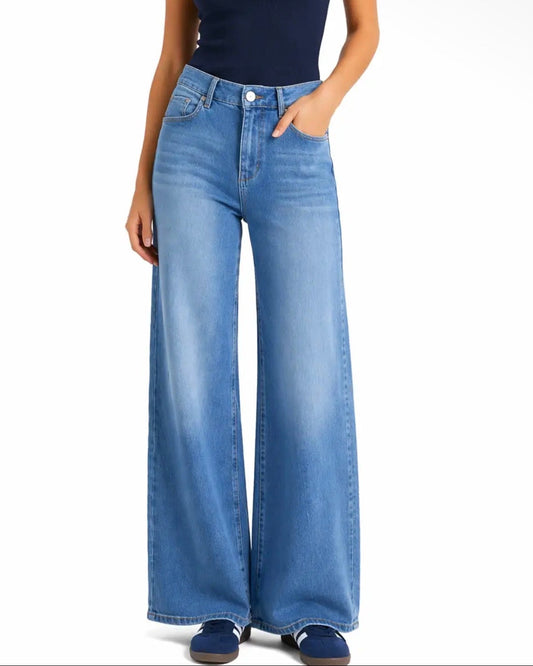 A woman modeling a navy blue square-neck tank top and high-waisted, wide-leg blue denim jeans against a plain white studio background.