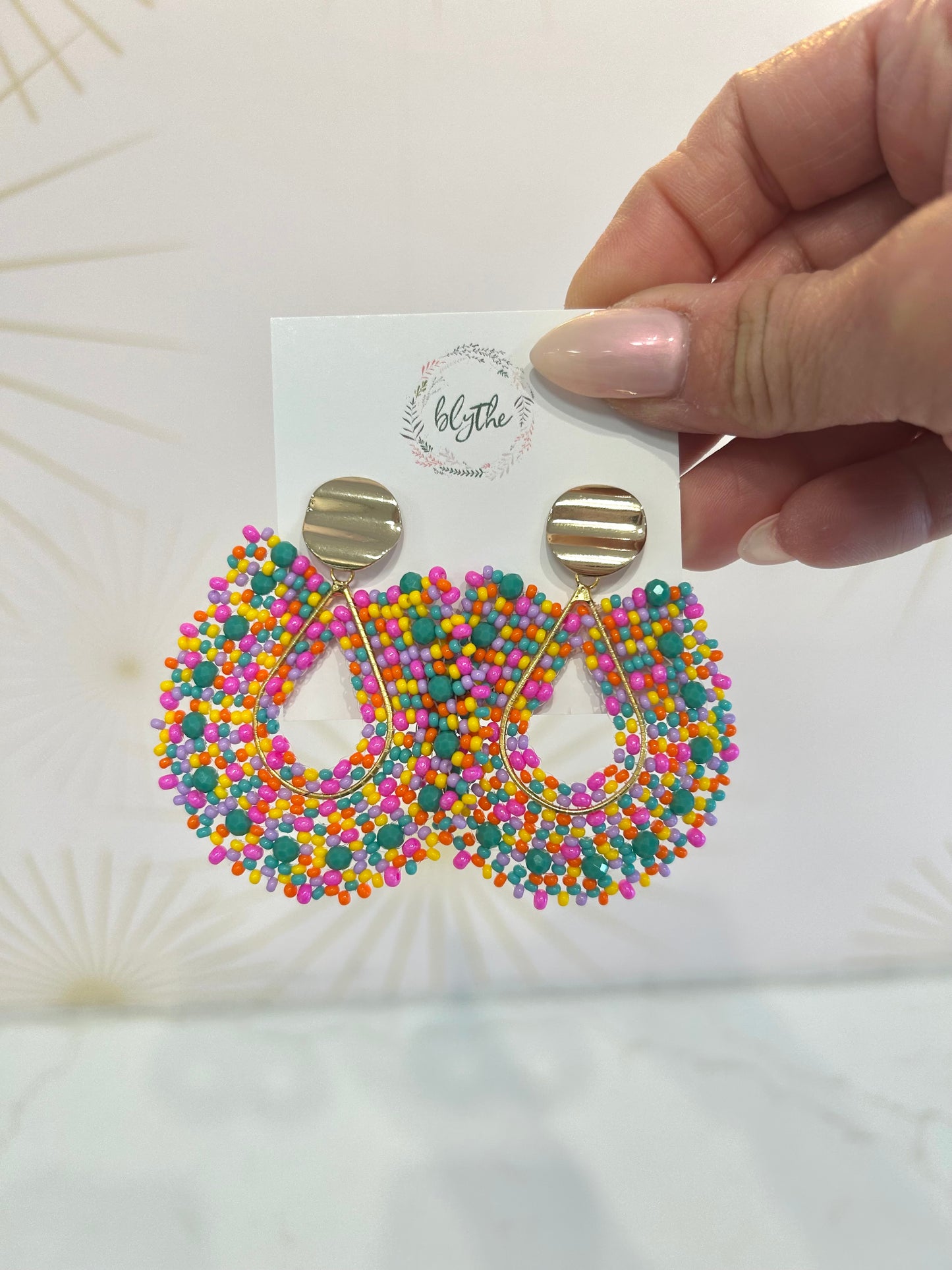 Colorful beaded earrings on a card held by a hand against a light background