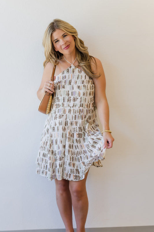 Woman in a patterned dress standing against a plain wall.